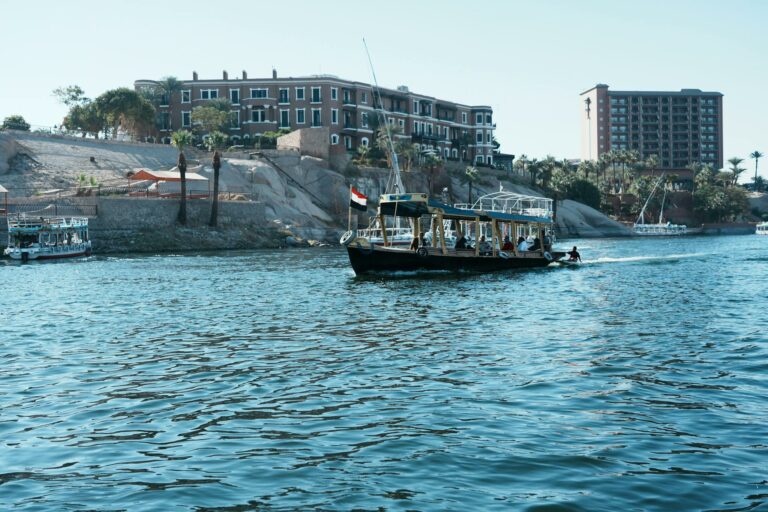 Scenic view of tour boats navigating the Nile River with architectural backdrop in Aswan, Egypt.